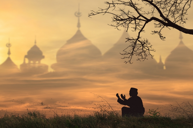 Muslim Man Praying Behind Blurred Mosque